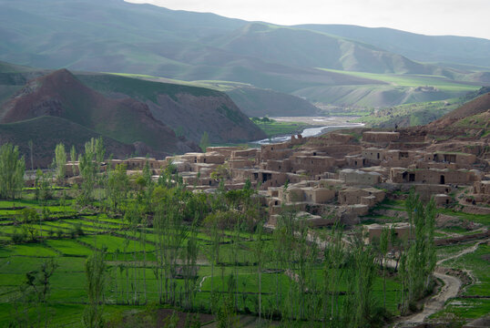Mud houses cluster above green fields in the village of Dera Jawal, along a river at the base of the Band-e Baba range,  Herat P