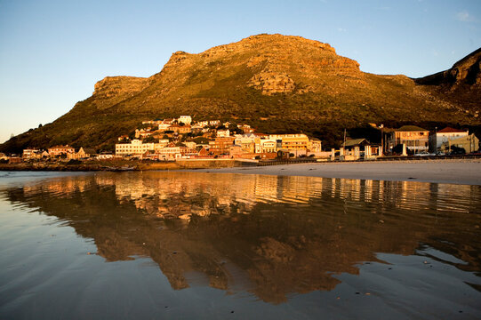 Sunrise forms a reflection of the small coastal town of Muizenberg on its beach in Cape Town, South Africa.