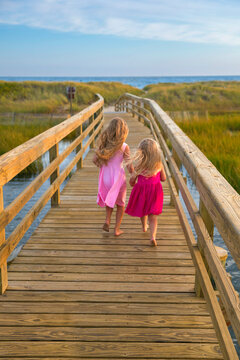 Little Girls From Behind Running On Bridge to Beach in Pink Dresses
