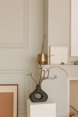 Dry branch in a modern black vase, blank picture frames near minimalistic decorative fireplace in modern Scandinavian interior. Copy space.