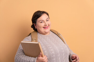 joyful college student holding academy book and smiling in studio shot. going to school, education,...