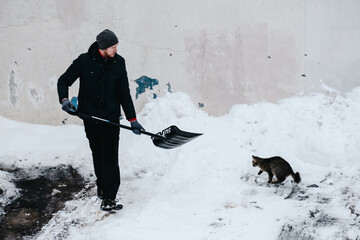 Snow removal in front of the house. The cat watches as the man cleans the snow