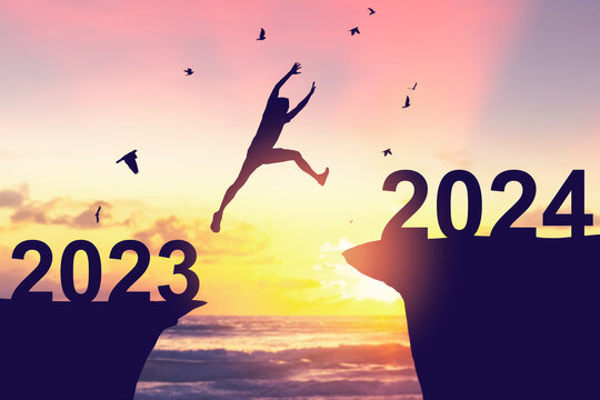 Silhouette man jumping between cliff with number 2023 to 2024 and birds flying at tropical sunset beach. Freedom challenge and travel adventure holiday concept.