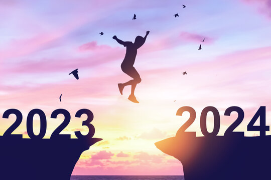 Silhouette man jumping between cliff with number 2023 to 2024 and birds flying at tropical sunset beach. Freedom challenge and travel adventure holiday concept.