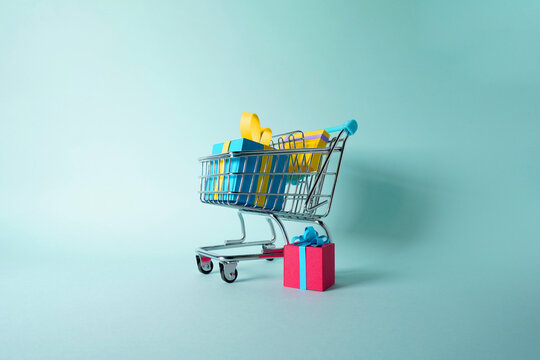 Shopping cart with a group of gifts and presents for Christmas, birthdays or Saint Valentine's Day made out of paper on a flat clean background. Trolley from bottom view