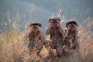 Three boy scouts exploring nature with binoculars in camp - obrazy, fototapety, plakaty
