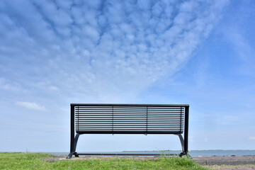 A long bench is placed in front of the beach. When the clear sky is full of clouds