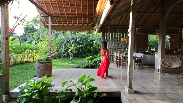 young asian girl in red maxi dress walking through open concept villa in Bali Indonesia