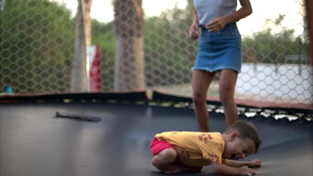 Slow motion of a latin toddler with a red short playing with his mother on a trampoline laughing and having fun