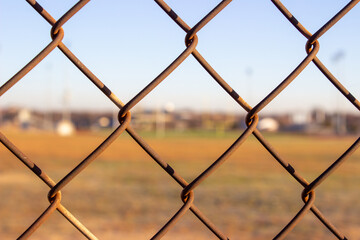 Rusty wire fence with field and buildings out of focus behind it