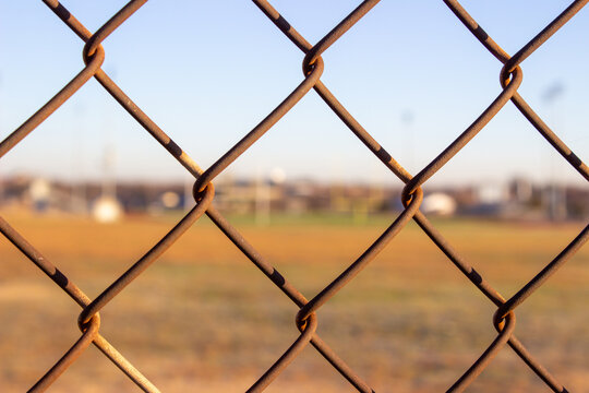 Rusty wire fence with field and buildings out of focus behind it