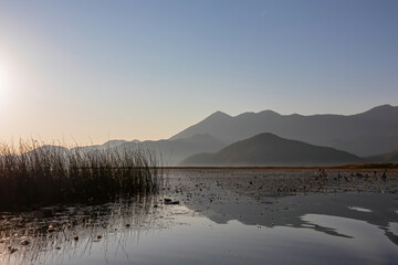 Panoramic view of Lake Skadar National Park in autumn at sunrise near Virpazar, Bar, Montenegro, Balkans, Europe. Stunning silhouette of mountains of Dinaric Alps reflecting on water surface, Albania