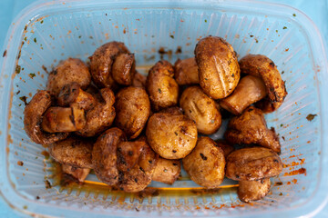 Whole pickled mushrooms in a plastic box close-up, picnic preparation.