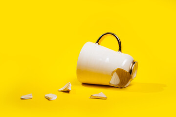 Broken tea cup isolated on yellow background. Cracked coffee mug and fragile ceramic pieces