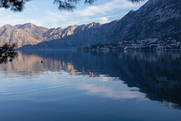 Panoramic view of bay of Kotor at sunrise in summer, Adriatic Mediterranean Sea, Montenegro, Balkans, Europe. Fjord winding along coastal towns. First sunbeams on Lovcen mountains. Water reflection