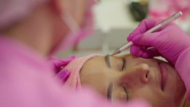make-up artist combing and styling eyebrows after the procedure of correction and coloring of eyebrows
