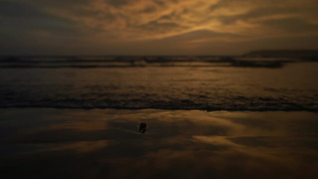 Beach with grey and gold sky reflecting on sand at dusk and waves calmly crashing at the shoreline 