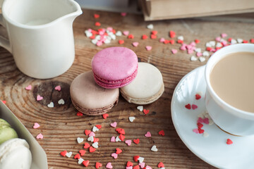 Macaroons and a cup of coffee, a milk jug on a background of small hearts on a wooden background, top view