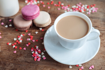 Fototapeta na wymiar Macaroons and a cup of coffee, a milk jug on a background of small hearts on a wooden background, top view
