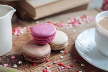 Macaroons and a cup of coffee, a milk jug on a background of small hearts on a wooden background, top view