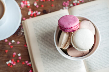 Macaroons in a bowl, a cup of coffee, on a background of small hearts on a wooden background