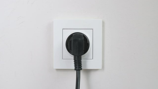 Male hand plugging and unplugging plug into white wall socket. Close-up power socket, caucasian man, charger cable