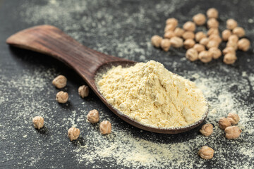Chickpea flour on the wooden spoon, on a black background, close up. Legumes. Organic food.