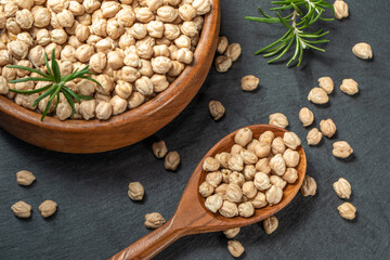 Dried raw chickpeas in wooden spoon and in wooden bowl, on a black background, closeup. Organic food. Legumes. Top view food.