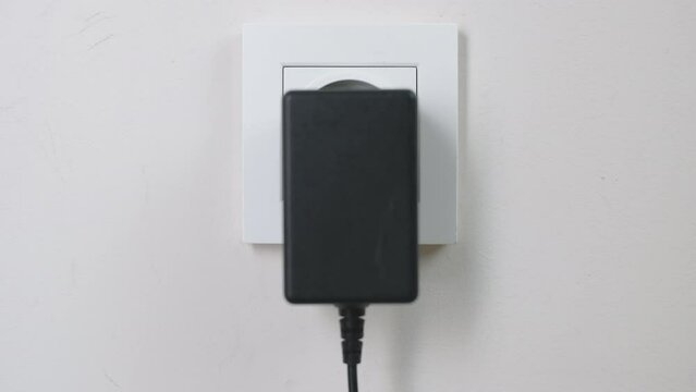 Male hand plugging and unplugging plug into white wall socket. Close-up power socket, caucasian man, charger cable