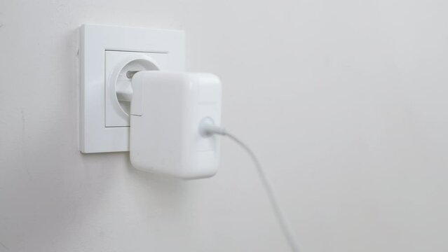 Male hand plugging and unplugging plug into white wall socket. Close-up power socket, caucasian man, charger cable