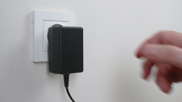 Male hand plugging and unplugging plug into white wall socket. Close-up power socket, caucasian man, charger cable