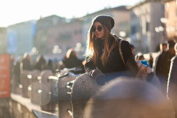 Young stylish blondie woman enjoying the Italian antic Roman Arena di Verona in trendy knitted hat,...