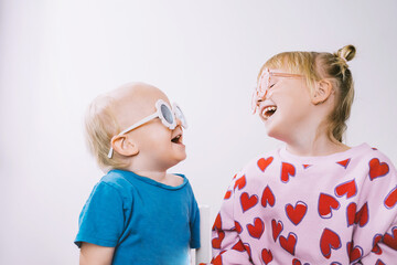 Happy little girl and boy laughing and posing in studio isolated over white background. Cheerful children wearing round flower sunglasses.