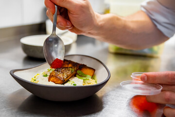chef hand cooking grilled salmon fish fillet with creamy ptitim, cheese and caviar