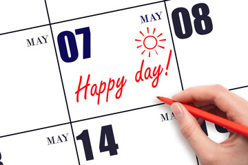 Hand writing the text HAPPY DAY and drawing the sun on the calendar date May 7