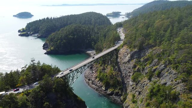 Cinematic descending dolly drone shot of deception pass bridge in washington wa usa. Smoky spring day with evergreen trees and turquoise water