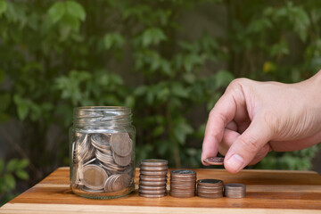 money saving hand in a jar, with natural lighting and coin on wooden table with green background, symbol of money saving for retirement