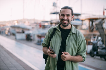 Naklejka premium Portrait of a young man with a phone in his hands in the city port of sailing and motor yachts on a sunny day.