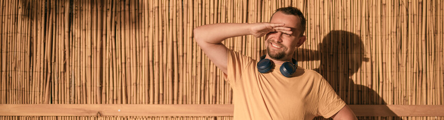 Portrait of a young guy in a yellow T-shirt against a yellow straw wall in bright sunlight.