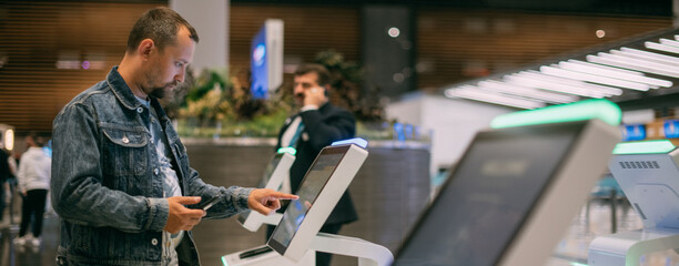A male passenger at the electronic check-in desk in the departure area of the modern airport terminal.
