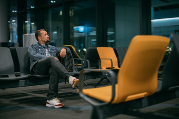 A male passenger is sitting waiting for boarding in the departure area of the modern airport terminal.