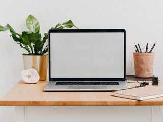 Wood desk with open laptop with white blank screen for text.