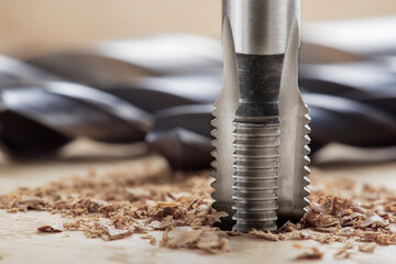 Thread tap drill cutting hole in wooden plate. Working cutter.