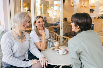 Three caucasian pretty senior women friends sitting with coffee at table in cafe terrace and smiling
