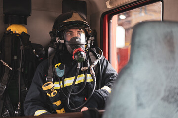 A young Spanish firefighter sitting in the uniformed fire truck, the man is in the back wearing a...