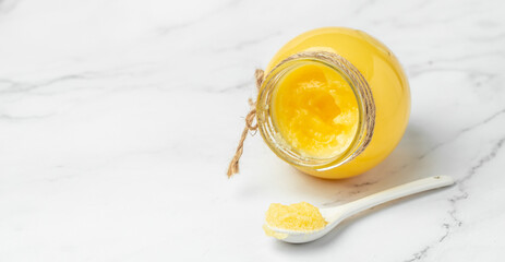 Pure OR Desi Ghee also known as clarified liquid butter in a bowl with wooden spoon on a light background. Long banner format