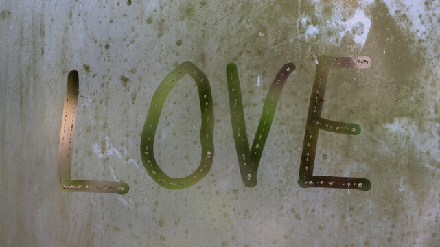 Word L O V E painted on a misted window. Symbol of love drawn on the glass.