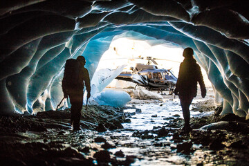 Adventurous couple emerge from an ice cave to find their helicopter.