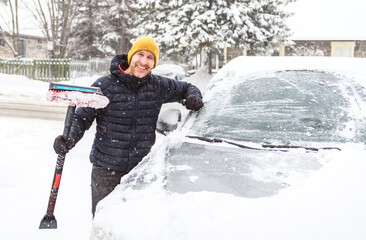 young man cleans his car after a snowfall on a sunny, frosty day