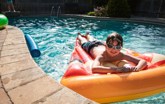 Young boy wearing goggles on a pizza float in a backyard pool.